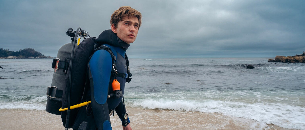 Austin Abrams as diver Jay Gardiner on a California beach in the 2026 film Whalefall; 20th Century Studios promotional still